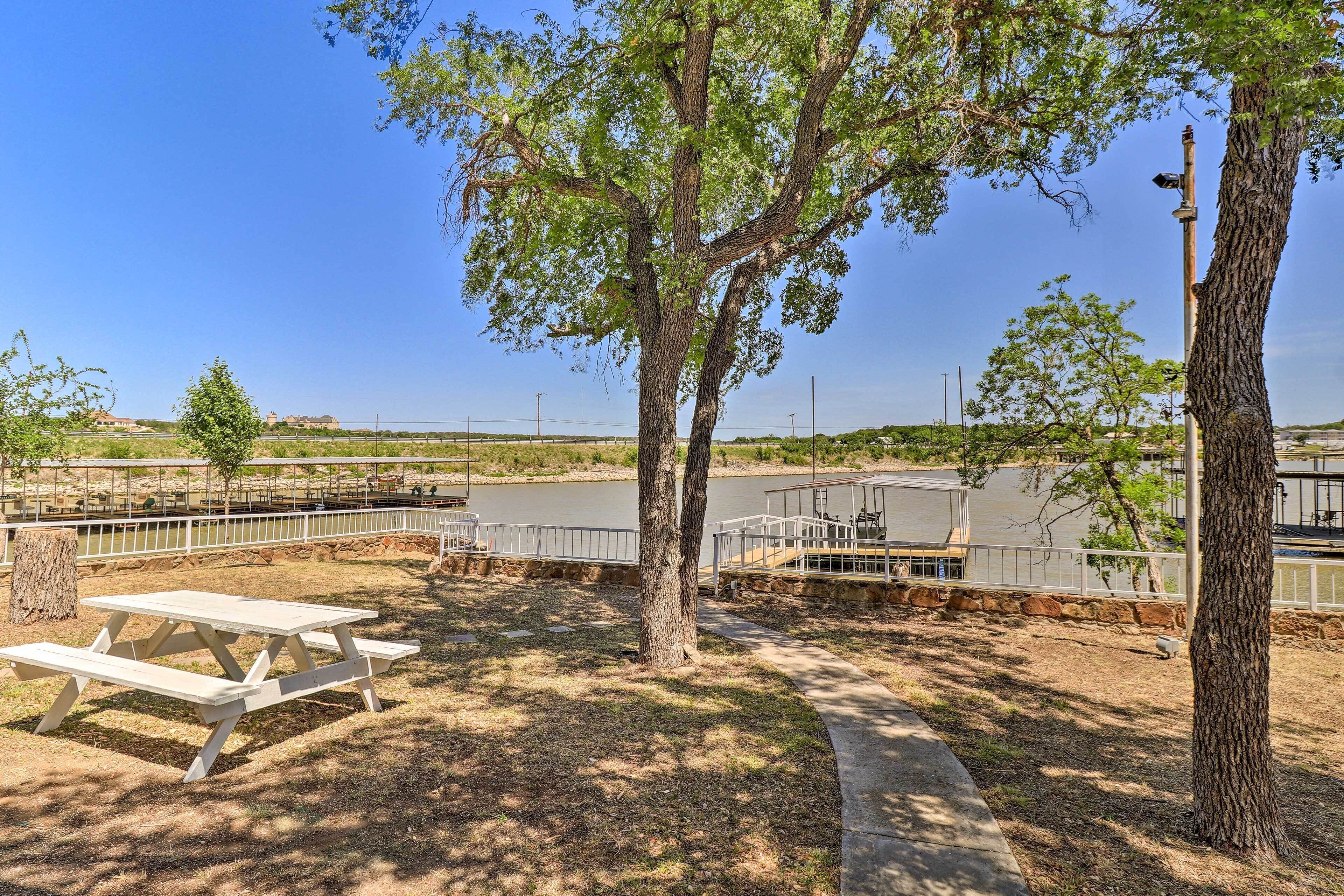 Una mesa de picnic y bancos en un parque con un lago y un puente al fondo.