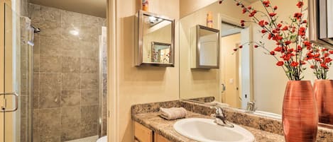 A bathroom with a glass shower enclosure, a sink, and a mirror.