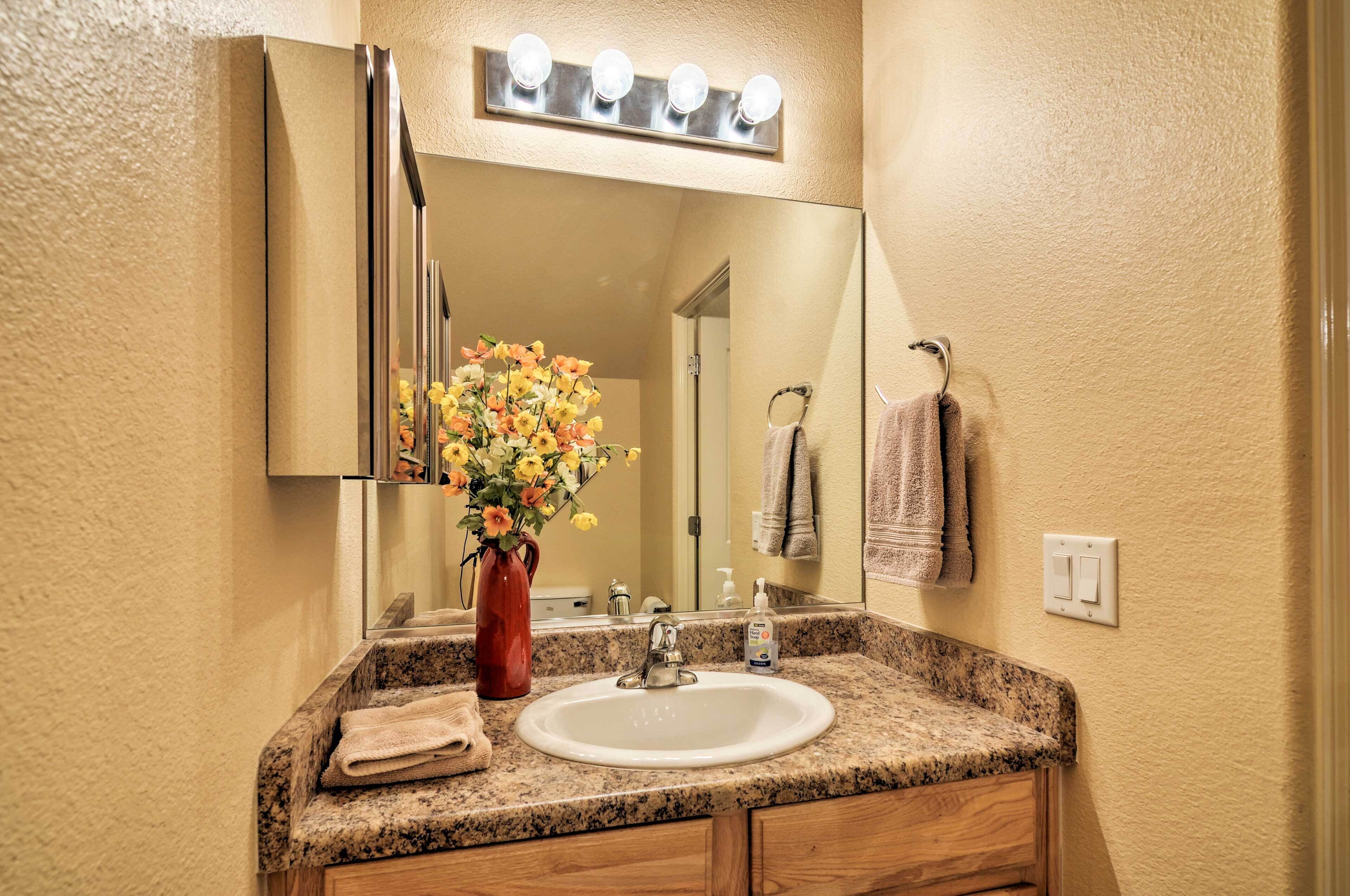 A bathroom with a granite countertop, white sink, and a mirror with lights above.