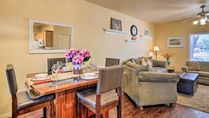 A dining area with a wooden table, chairs, and a vase of flowers. There is a sofa and a lamp in the living area.