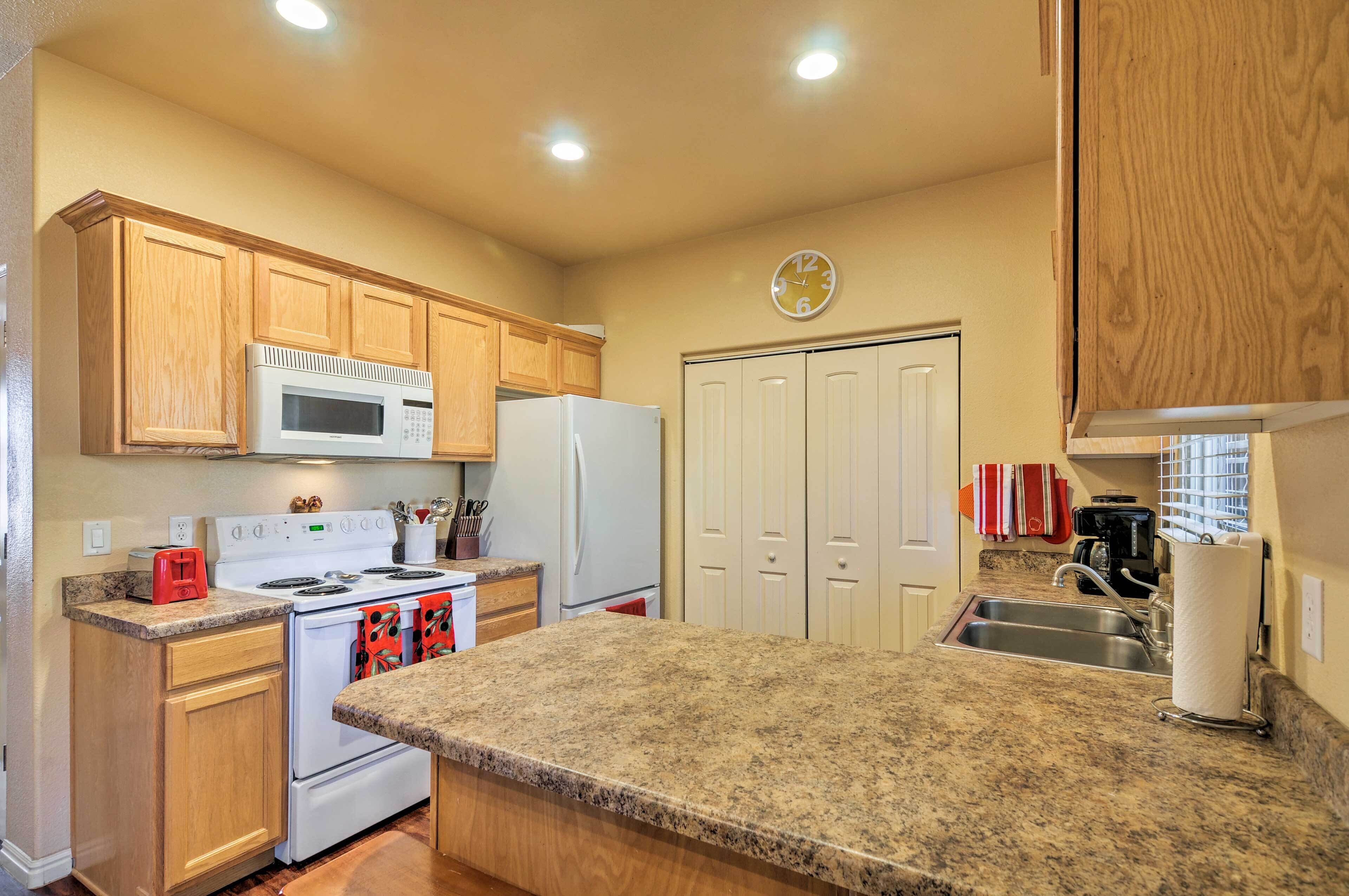 A kitchen with wooden cabinets, a microwave, a stove, a refrigerator, and a clock on the wall.