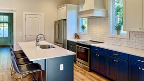 A modern kitchen with a central island, stainless steel appliances, and dark cabinetry. - Luxe Lakefront Getaway w/ Porch + Water View! (Dadeville)