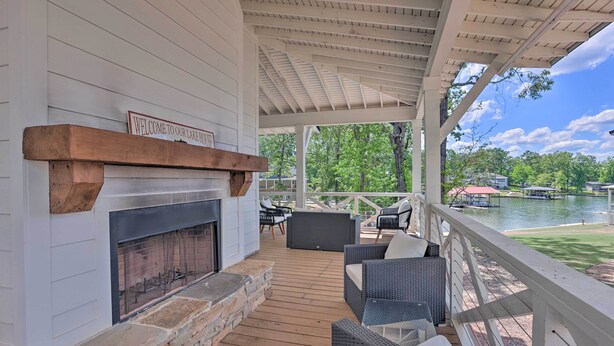 A covered outdoor deck with a fireplace, wicker furniture, and a view of a lake. - Luxe Lakefront Getaway w/ Porch + Water View! (Dadeville)