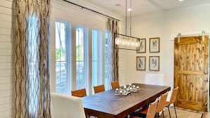 A dining area with a wooden table, six chairs, a chandelier, and a wooden door. - Luxe Lakefront Getaway w/ Porch + Water View! (Dadeville)