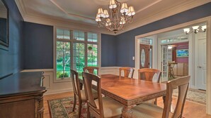 A dining room with a wooden table and chairs, a chandelier, and a view of the outdoors through large windows. - Tellico Village Getaway w/ Theater, Game Room (Loudon)