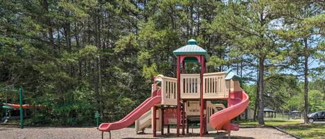 A playground with two slides and a climbing structure surrounded by trees.