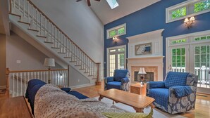 A spacious living room with a wooden staircase, a fireplace, and two blue armchairs. - Tellico Village Getaway w/ Theater, Game Room (Loudon)