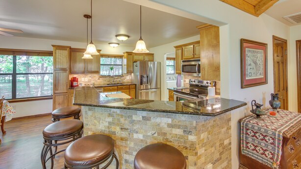 A spacious kitchen with a large island, bar stools, wooden cabinets, and a stone backsplash. - Dog-friendly Wills Point Home w/ Grill on 10 Acres (Wills Point)