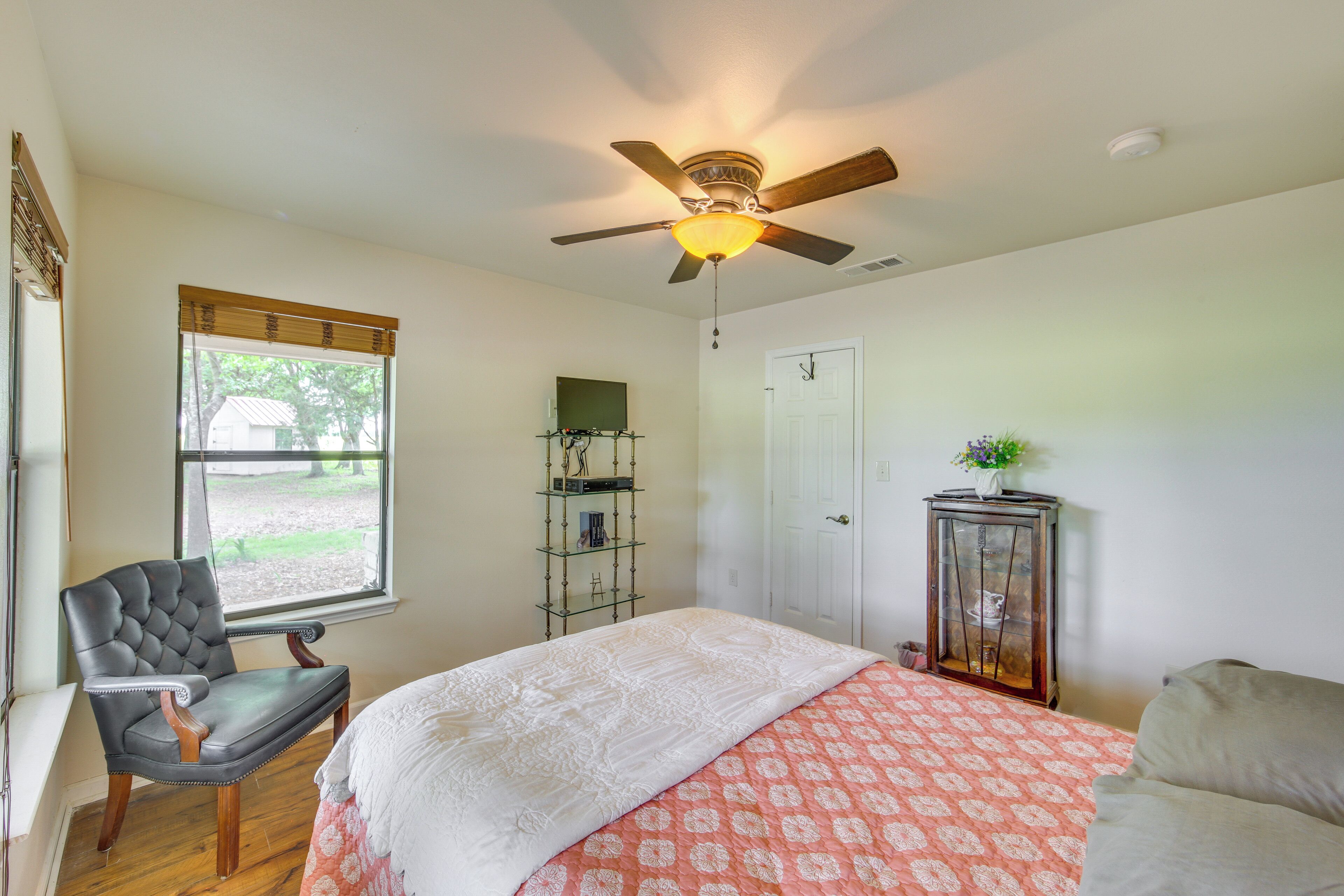 A bedroom with a bed, a chair, a ceiling fan, a window, and a door.