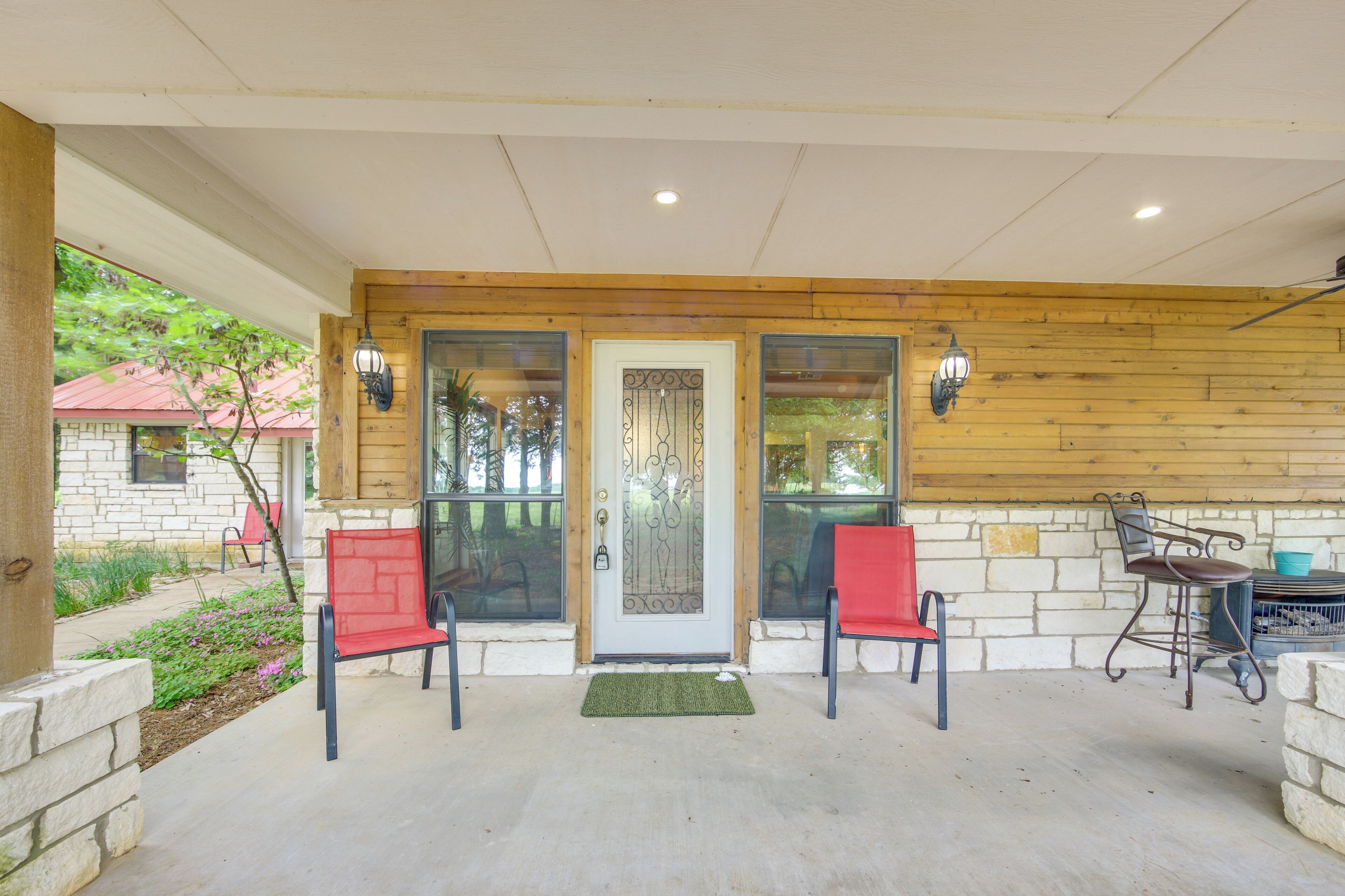 A covered porch with two red chairs, a wooden wall, and a door with a glass panel.
