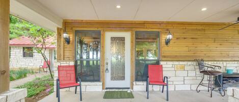 A covered porch with two red chairs, a wooden wall, and a door with a glass panel.