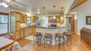 A modern kitchen with wooden cabinets, a central island with stools, a ceiling fan, and pendant lighting. - Dog-friendly Wills Point Home w/ Grill on 10 Acres (Wills Point)