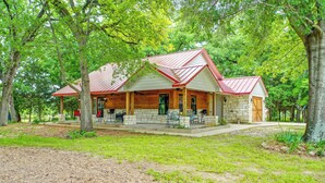 A lodge with a stone exterior, a red roof, and a covered porch with outdoor seating. - Dog-friendly Wills Point Home w/ Grill on 10 Acres (Wills Point)