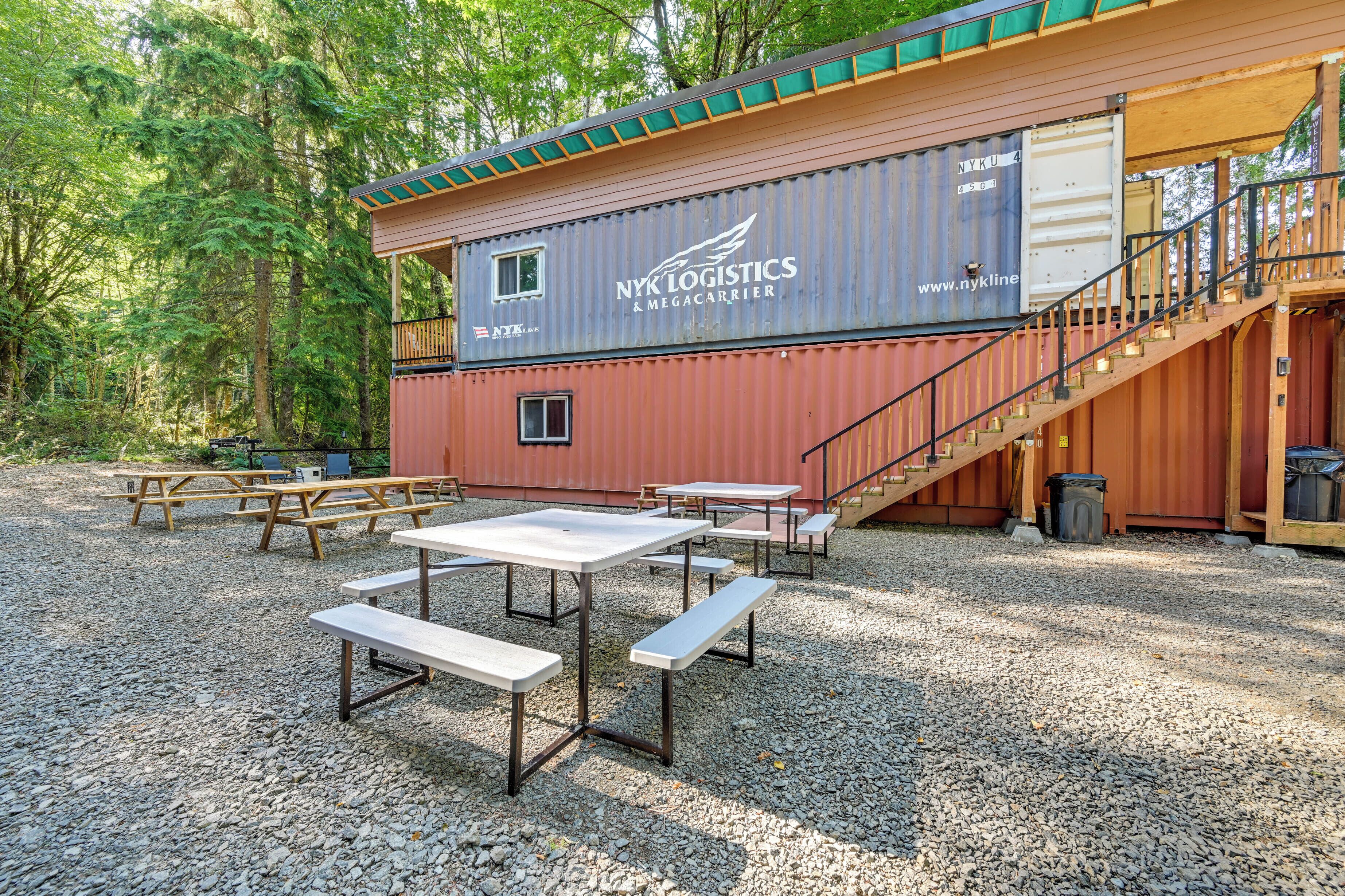 A rustic cabin with a wooden exterior and a shipping container as the main building. There are picnic tables and benches outside.