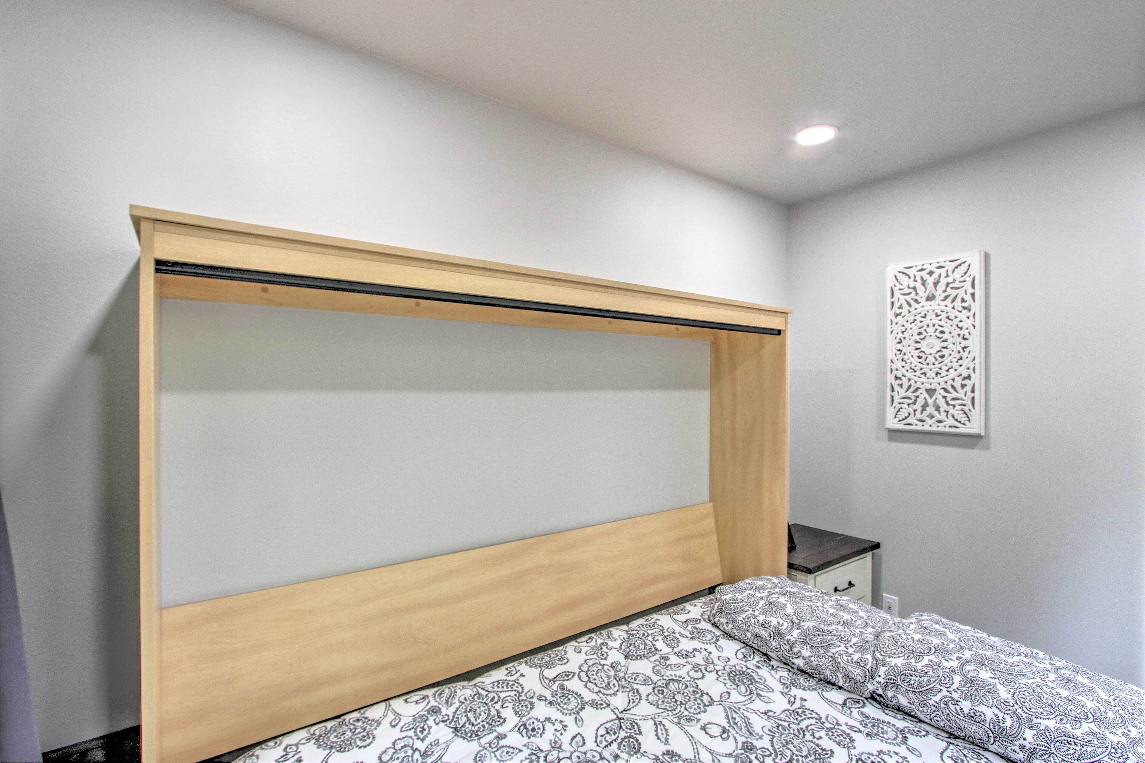 Un dormitorio con cabecera de cama de madera, colcha estampada, mesita de noche y un adorno en la pared.