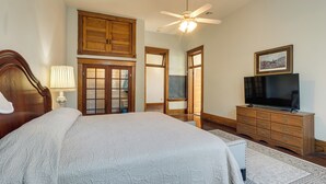 A bedroom with a large bed, wooden wardrobe, ceiling fan, and a television on a dresser.