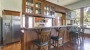 A kitchen with wooden cabinets, a stainless steel refrigerator, and a bar area with chairs.