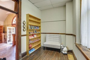 A library with wooden bookshelves, a cushioned bench, and a door leading to another room. - Renovated Schoolhouse w/ Piano & Private Deck! (Florence)