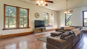 A spacious living room with hardwood floors, a large sectional sofa, a television on a wooden stand, and a ceiling fan.