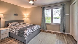 Een slaapkamer met een bed, bedlampen, een plafondventilator, een raam met gordijnen en een nachtkastje.