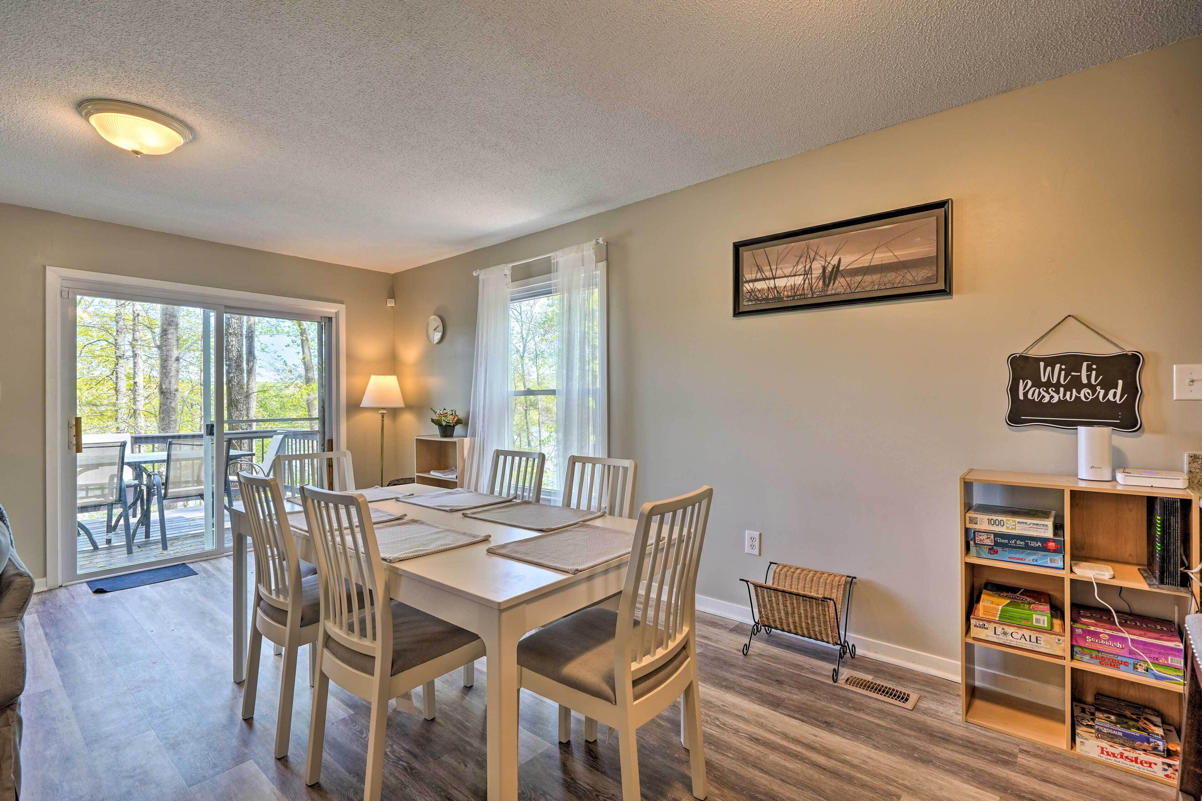 A dining area with a table set for six, a bookshelf with board games, and a Wi-Fi password sign on the wall.