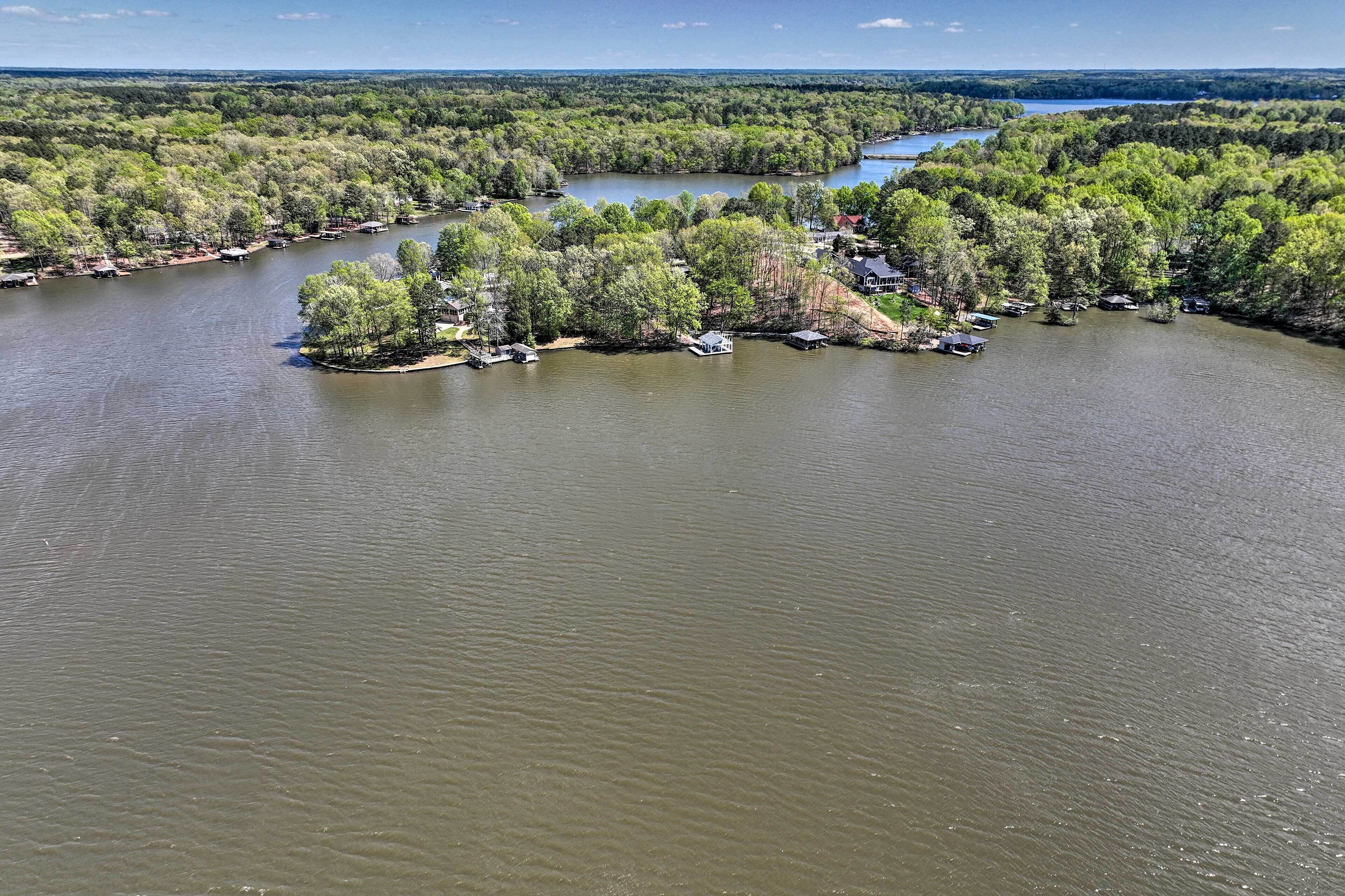 An aerial view of a lakeside property with a dock, boats, and cabins surrounded by dense forest.