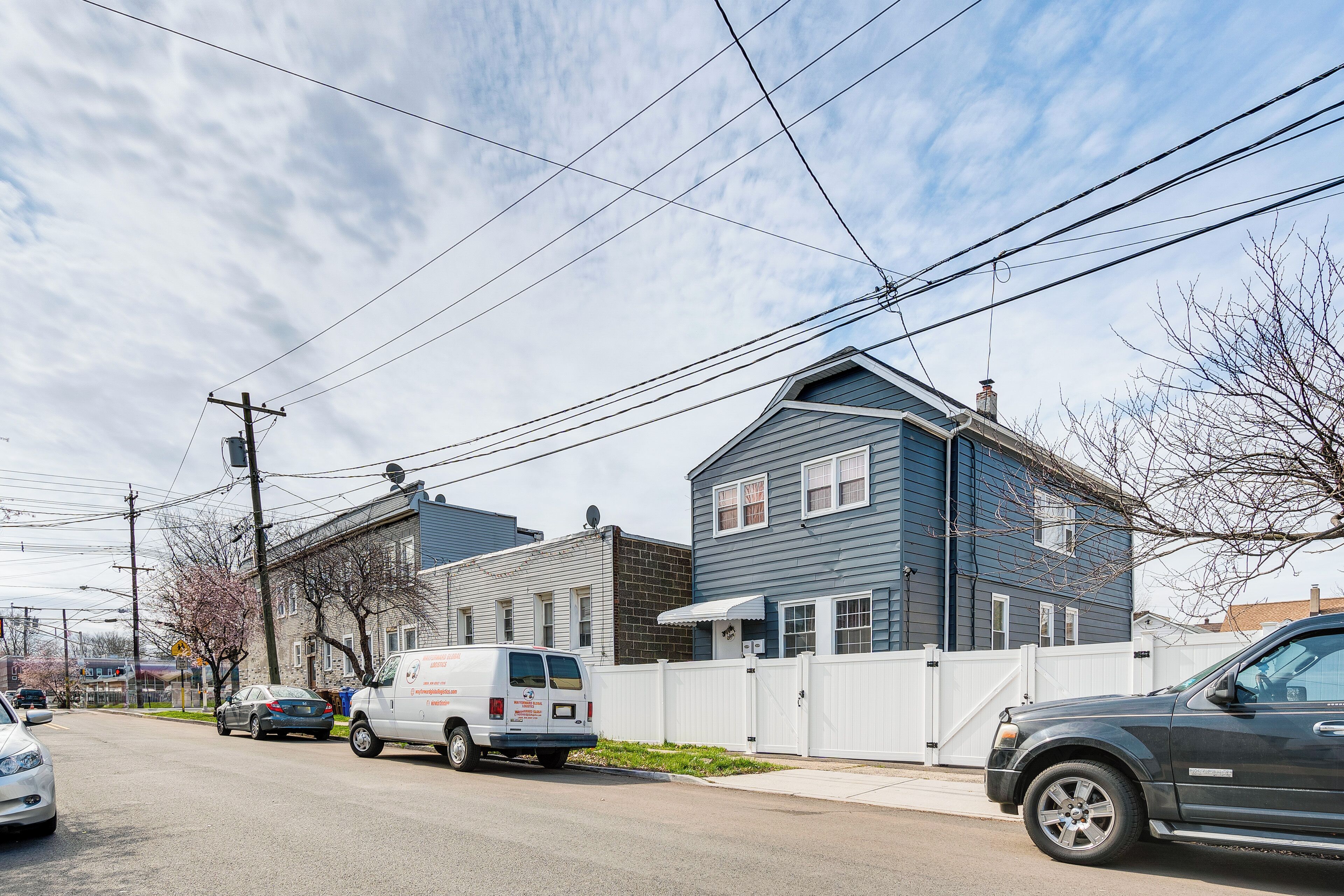 A street view with a two-story house, a white fence, and a parked van.