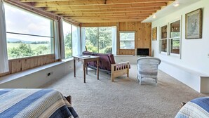 Une pièce chaleureuse avec un plafond en bois, de grandes fenêtres, un canapé, un fauteuil et un téléviseur.