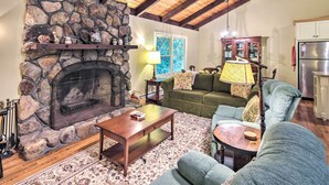 Uma sala de estar acolhedora com lareira de pedra, vigas de madeira, um sofá verde e uma mesa de jantar.