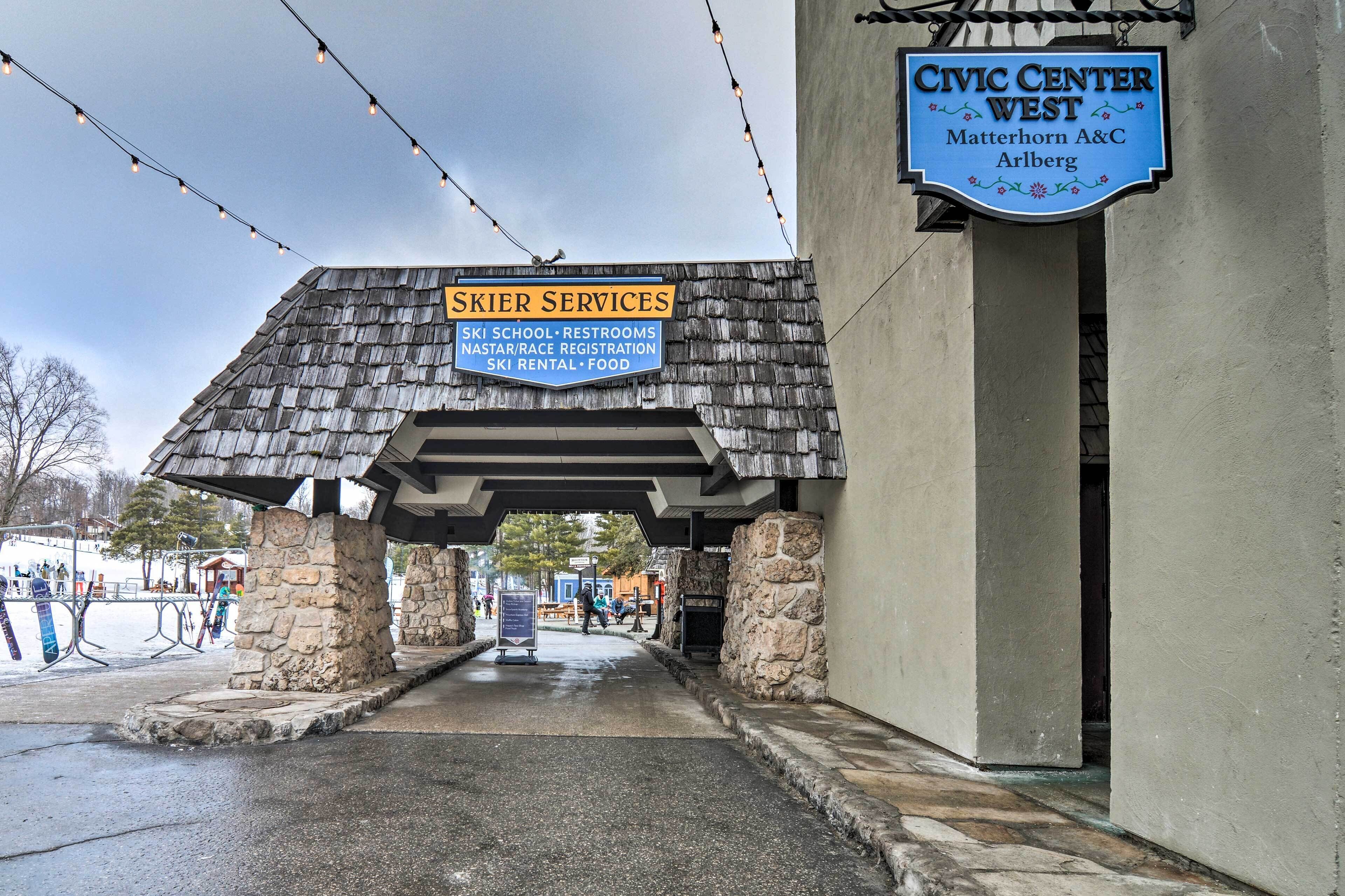 Entrada de un edificio con letreros que indican Centro Cívico West, Matterhorn A&C y Arlberg, y un cartel de Servicios para Esquí que enumera comodidades como escuela de esquí, baños y comida.