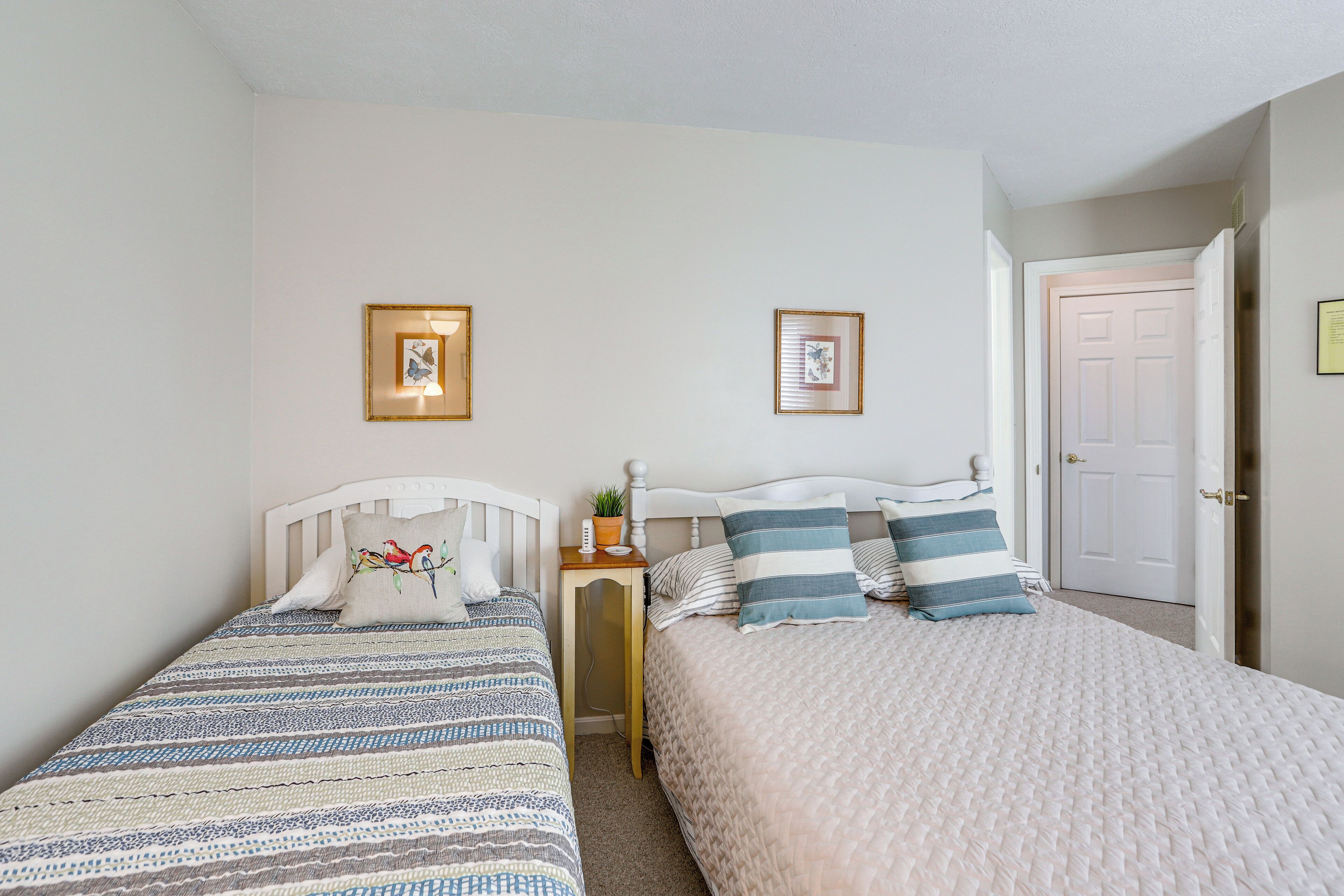 A bedroom with two beds, each with different bedding patterns, a small table with a lamp, and framed pictures on the wall.