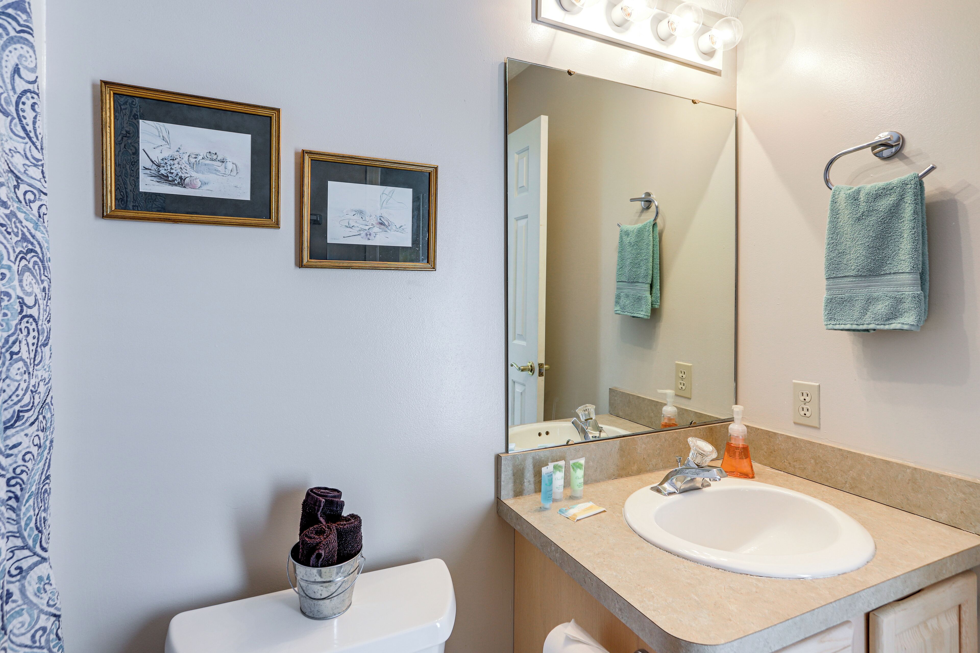 Une salle de bain avec un lavabo blanc, un miroir avec éclairage intégré et deux tableaux encadrés accrochés au mur.
