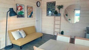 Une pièce chaleureuse avec un canapé jaune, une table à manger avec des chaises, une échelle et des œuvres d’art accrochées au mur.