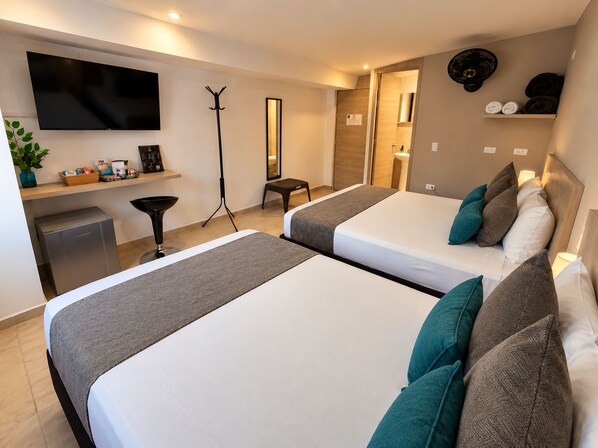 Una habitación de hotel con dos camas, televisión, escritorio, espejo y una pequeña kitchenette.