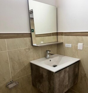 Un baño con un lavamanos blanco, un espejo encima y un perchero para toallas.