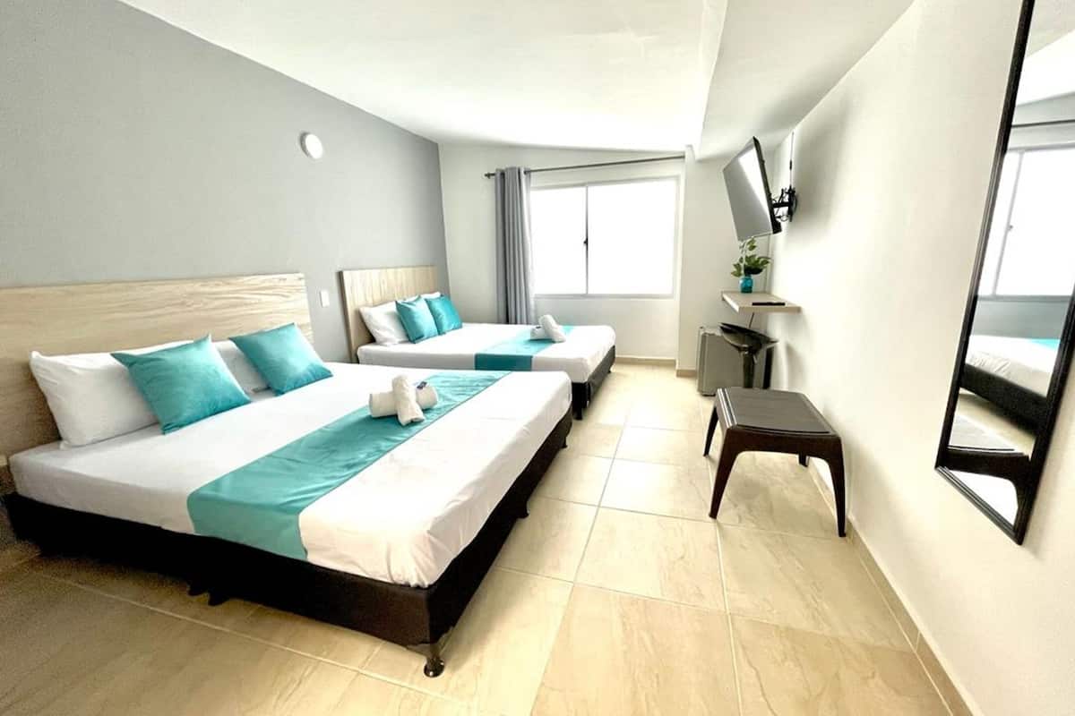Quarto de hotel com duas camas, televisão, uma mesa pequena e janela com cortinas.