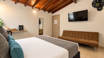 Una habitación de hotel con cama, sofá, televisión, espejo y repisa con objetos.