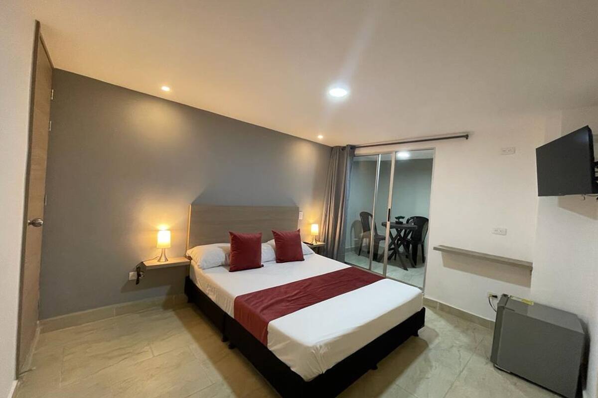 Quarto de hotel moderno com uma cama grande, luminárias laterais, televisão de tela plana e porta de vidro deslizante que dá para uma varanda.