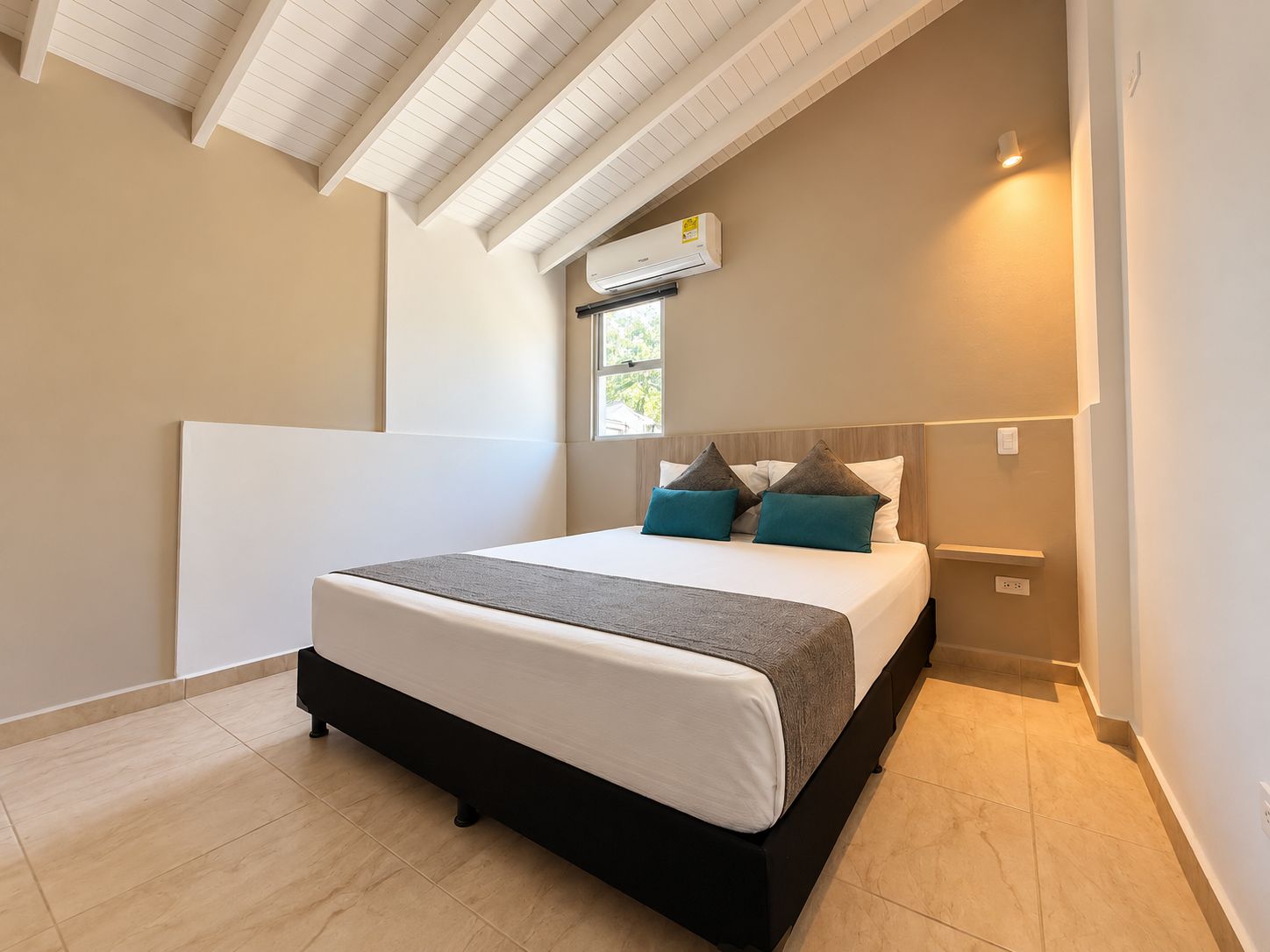 A bedroom with a bed, a window, an air conditioning unit, and a light fixture.