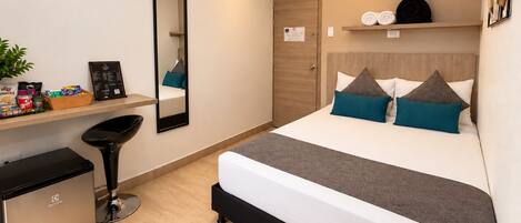 A modern hotel room with a bed, bedside table, mirror, and a small kitchenette.