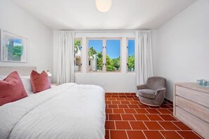 Une chambre à coucher avec un grand lit, une chaise, une commode et une fenêtre avec des rideaux.