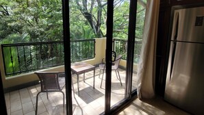 A balcony with a view of a lush garden, a table with chairs, and a refrigerator. - 4th floor Apartment - 2 minutes walking distance to the beach! (Tamarindo)