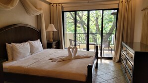 A bedroom with a large bed, a nightstand, a lamp, and a view of a balcony with chairs. - 4th floor Apartment - 2 minutes walking distance to the beach! (Tamarindo)