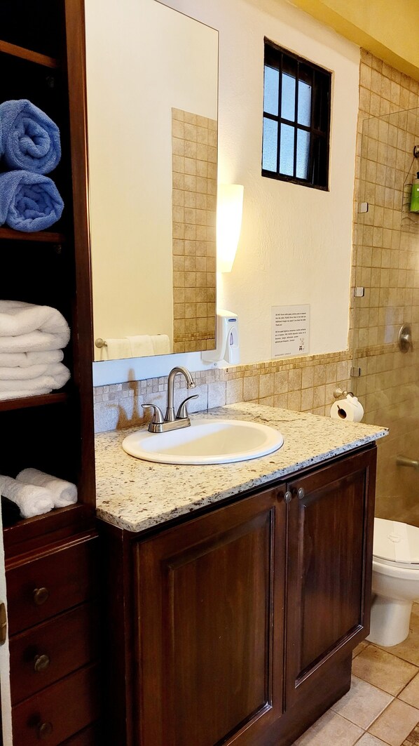 Un baño con lavamanos, espejo, toallero y ventana.