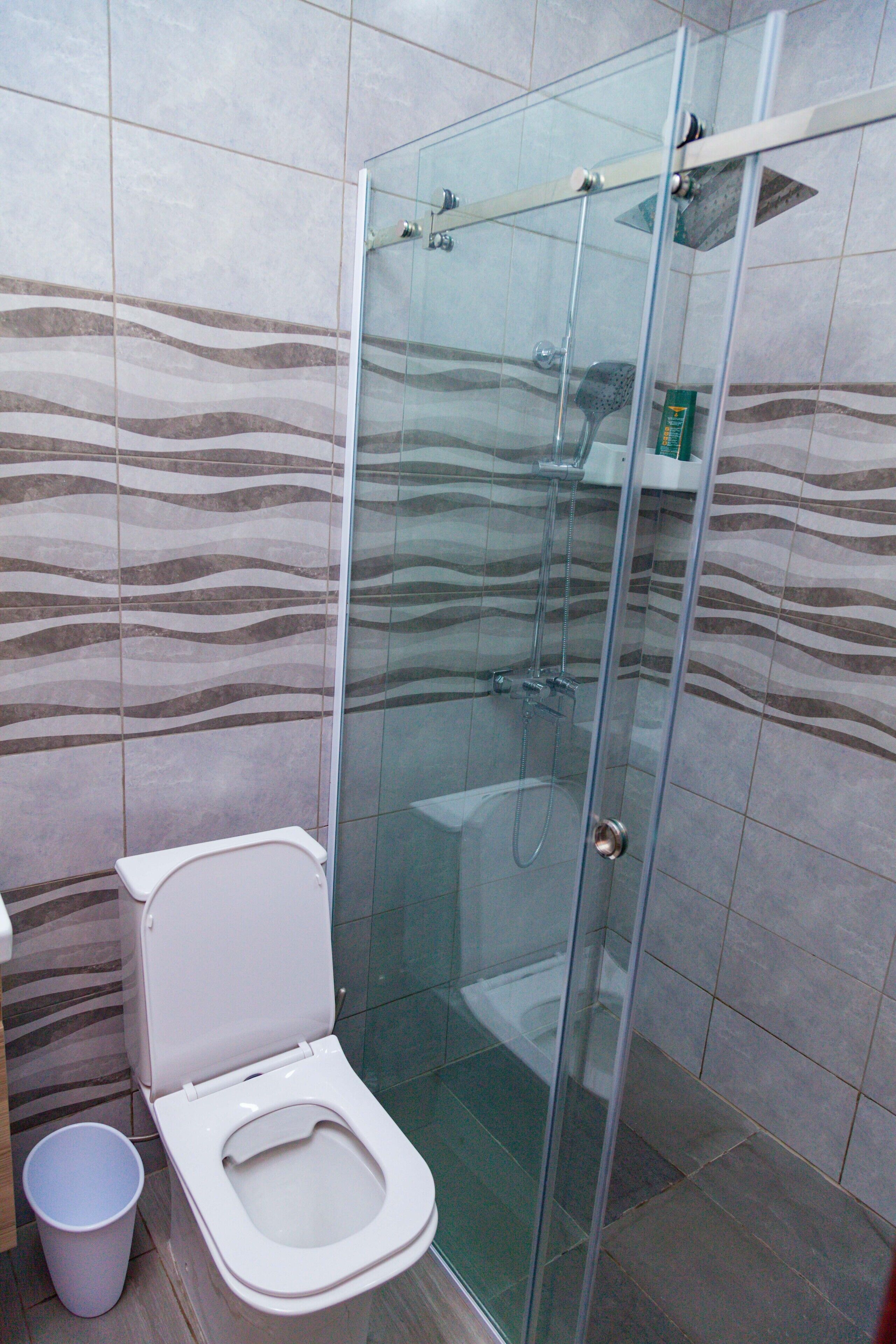 Une salle de bain avec une douche à parois de verre, des toilettes et une poubelle.