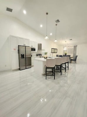 Una cocina moderna con armarios blancos, un refrigerador de acero inoxidable e iluminación colgante.
