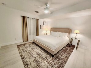 Un dormitorio con una cama, dos mesitas de noche, un ventilador de techo y una alfombra estampada.