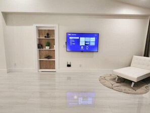 Una sala de estar moderna con un televisor de pantalla plana montado en la pared, un sofá blanco y un estante de madera con objetos decorativos.