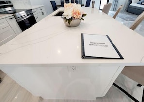 Una cocina moderna con muebles blancos, un horno de acero inoxidable y una zona de comedor con mesa y sillas blancas.