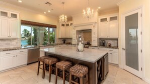 A spacious kitchen with white cabinetry, a large island with stools, and a view of the outdoors.